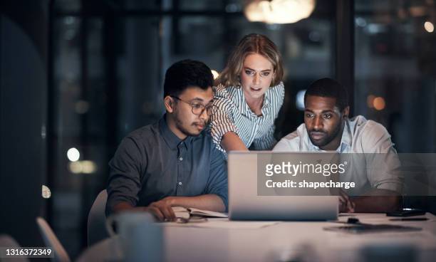 skott av ett team av unga affärsmän som använder en bärbar dator under ett sent nattmöte på ett modernt kontor - meeting man woman bildbanksfoton och bilder