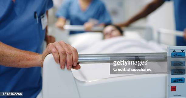 abgeschnittener schuss eines nicht wiederzuerkennenden medizinischen teams, das einen patienten in einem krankenhausbett durch den flur der station schiebt - unconscious stock-fotos und bilder