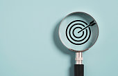Target board inside of magnifier glass for focus business objective on blue background and copy space.