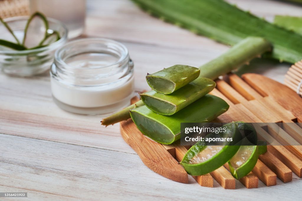Aloe vera slices and moisturizer on a wooden table. Beauty treatment concepts