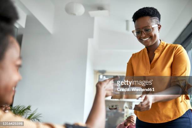 smiling female entrepreneur offering coffee to female colleague at coworking office - tray stock pictures, royalty-free photos & images