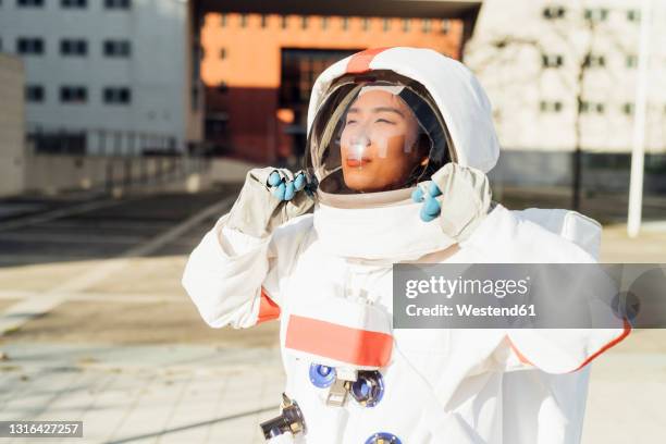 female astronaut holding helmet while standing outdoors during sunny day - space helmet stock pictures, royalty-free photos & images