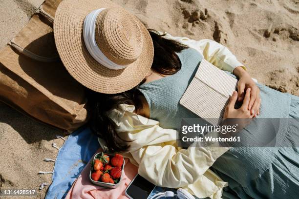 woman covering face with hat while lying on beach - woman face hat foto e immagini stock
