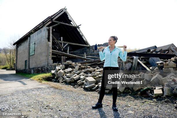 thoughtful woman standing with hammer on road with destructed house in background - ruined clothes stock pictures, royalty-free photos & images