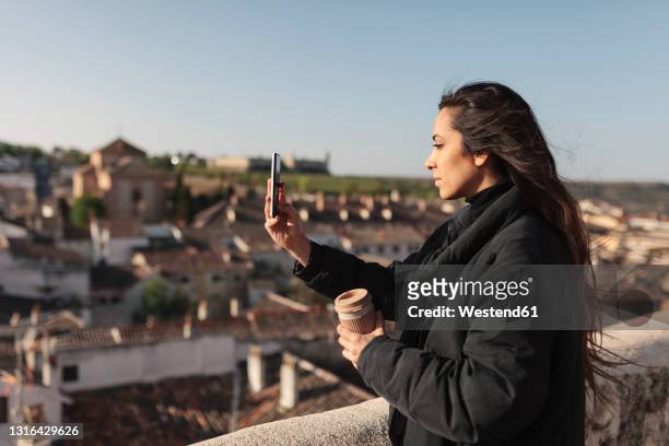 young woman taking selfie through mobile phone while standing at rooftop - provinz toledo stock-fotos und bilder