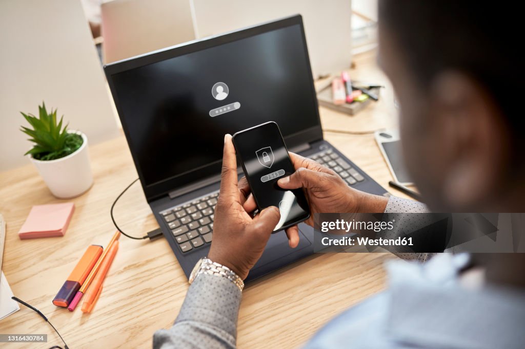 Businessman protecting data while using smart phone over laptop at office