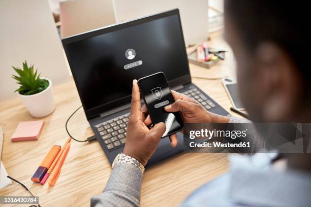 businessman protecting data while using smart phone over laptop at office - data privacy foto e immagini stock