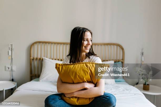 smiling woman embracing pillow on bed at home - pillows for sitting up in bed stock pictures, royalty-free photos & images