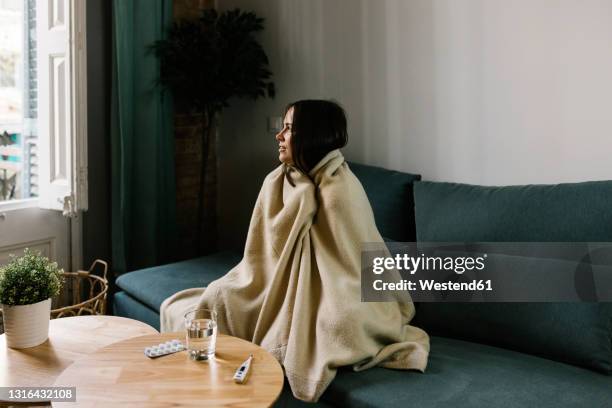 sick woman looking away while wrapped in blanket at home - blocked nose stock-fotos und bilder