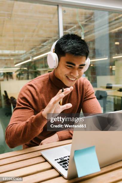 smiling male entrepreneur waving hand during video call on laptop at cafeteria - zwaaien gebaren stockfoto's en -beelden