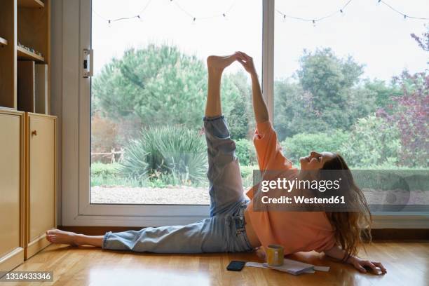 smiling woman stretching legs while lying on side at home - dar uma ajuda imagens e fotografias de stock