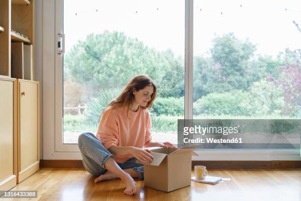 beautiful woman opening cardboard box while sitting at home - online shopping opening package stock pictures, royalty-free photos & images