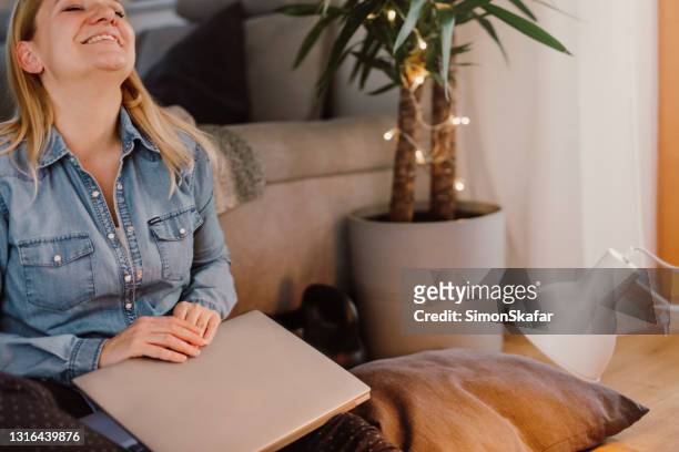 satisfied woman sitting with laptop in living room - closed laptop stock pictures, royalty-free photos & images