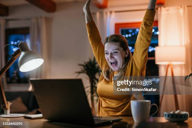 smiling woman with arms raised sitting in front of laptop - sports betting stock pictures, royalty-free photos & images