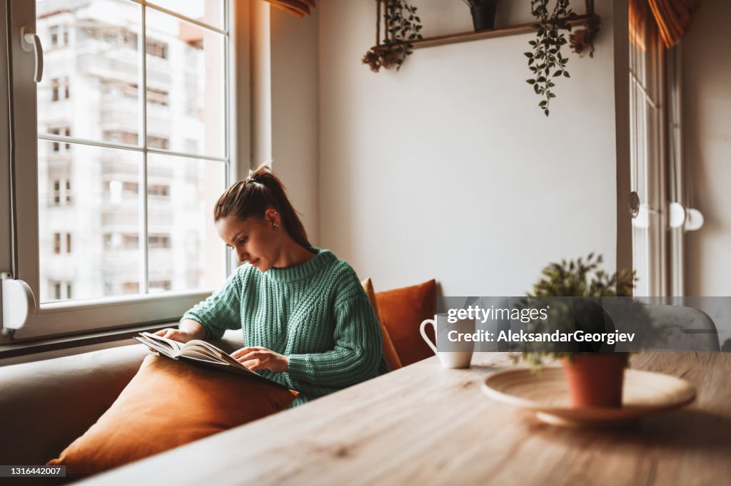 Female Looking At Old Photo Album In Home Kitchen