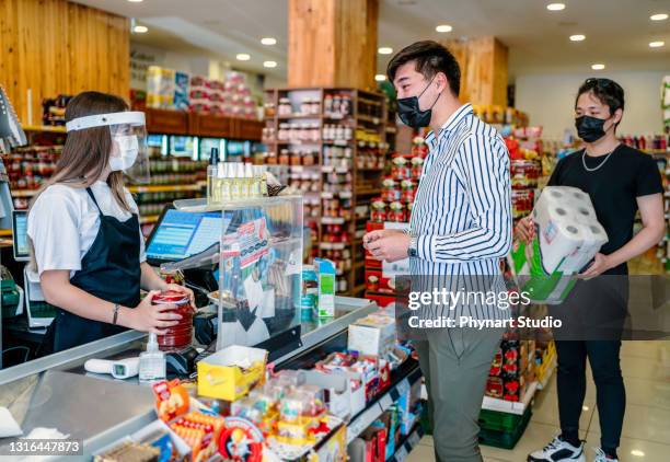 kassier of supermarktpersoneel in medisch beschermend masker en gezichtsschild dat bij supermarkt werkt. covid-19 verspreiding uitbraak - convenience store counter stockfoto's en -beelden