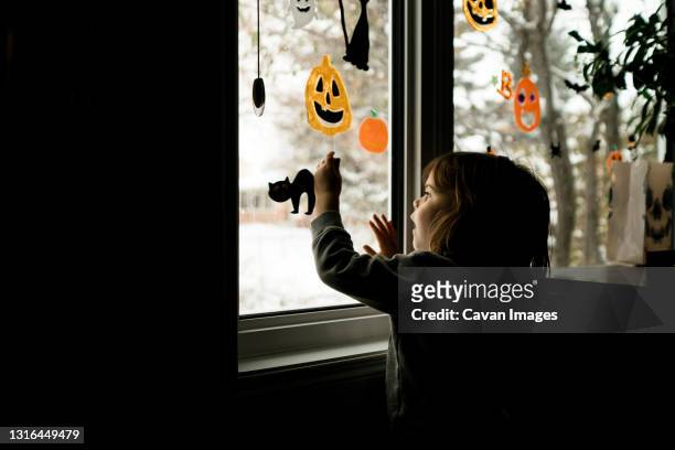 young girl putting halloween decorations up on windows in living room - pumpkin cats fotografías e imágenes de stock