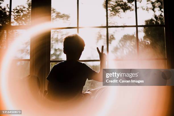 back of young boy in window making peace sign with circle light effect - flash back stock pictures, royalty-free photos & images