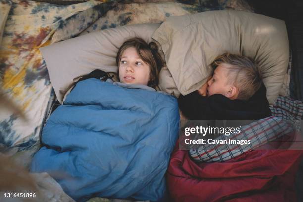 two friends side by side in sleeping bags. one looks scared. - scared boy imagens e fotografias de stock