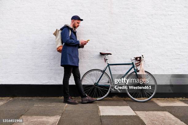 man with bicycle using smart phone while leaning on wall - phone leaning stock pictures, royalty-free photos & images