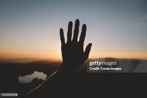 woman's hand silhouetted against the western sky and distant lake - end of life stock pictures, royalty-free photos & images