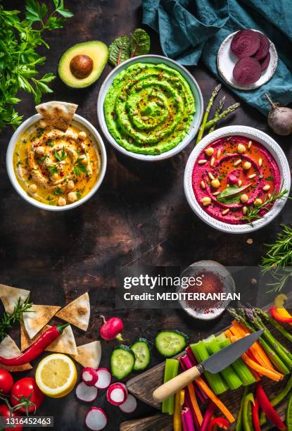 hummus drei schüssel kichererbsen, avocado und rote bete mit geschnittenem gemüse stäbchen auf dunklem holztisch - lebanese food stock-fotos und bilder