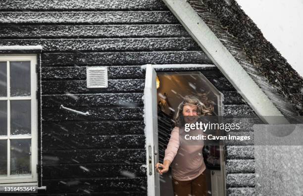 woman holding door open with hair blowing in snow storm in denmark - hygge stockfoto's en -beelden