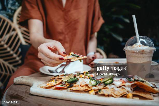 close up of young asian woman sitting on a rattan armchair at sidewalk cafe, enjoying meal and eating freshly served nacho chips. eating out lifestyle - female eating chili bildbanksfoton och bilder