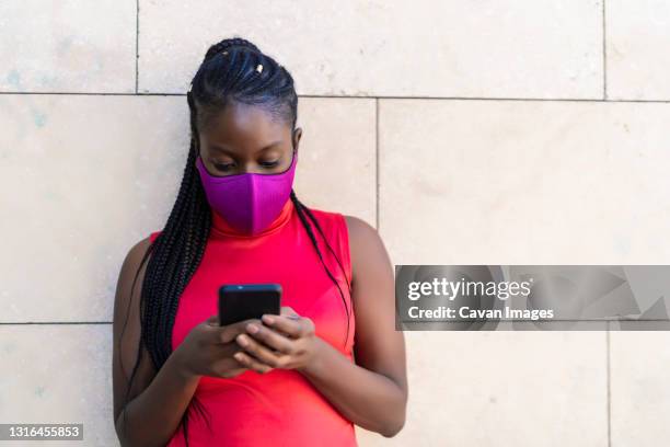 woman with african braids sending a message from her smartphone - lateral portrait looking mobile photos et images de collection