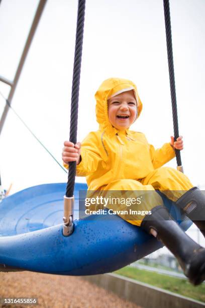 happy toddler boy rides on swing at the park on a wet day - schaukel regen stock-fotos und bilder