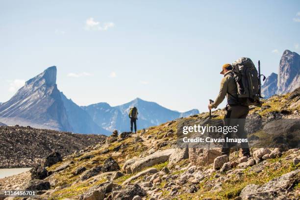 backpackers hike over rocky terrain in akshayak pass. - mount thor stock pictures, royalty-free photos & images
