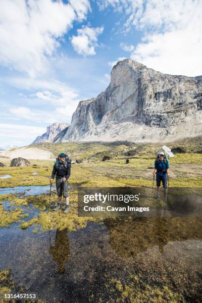 two backpackers stand below mount thor. - mount thor stock pictures, royalty-free photos & images