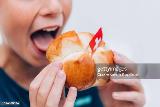 close up of a young boy taking a bite of traditional swiss bread. - 1 august schweiz stock-fotos und bilder