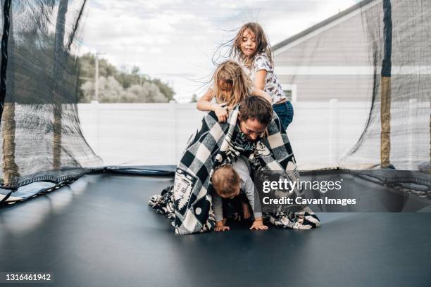 three kids climbing on dad while they play on a trampoline at home - trampoline stock-fotos und bilder