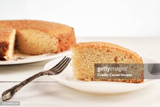 close up of a slice of homemade sponge cake on a white wooden table - sponge cake stock-fotos und bilder