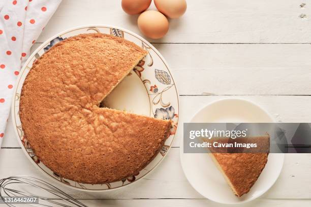 homemade sponge cake cut into slices and eggs on a white wooden table - sponge cake stock-fotos und bilder