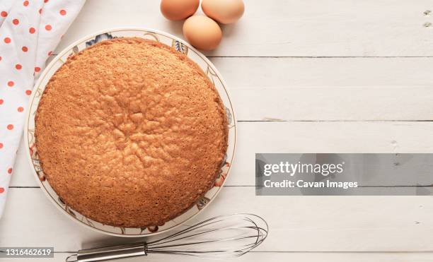 top view of a homemade sponge cake and eggs on a white wooden table - torta foto e immagini stock