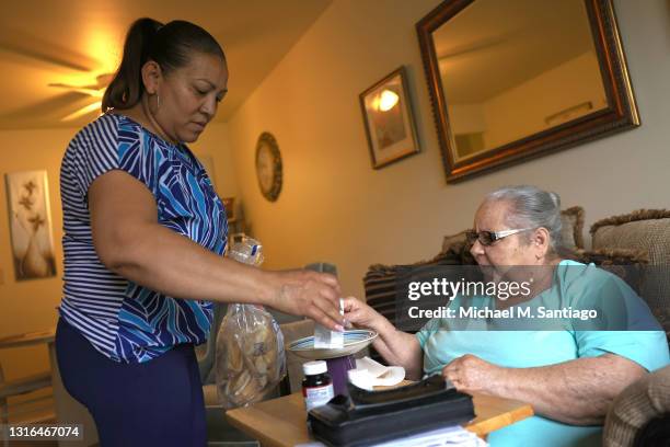 Lidia Vilorio, a home health aide, gives her patient Martina Negron her medicine and crackers for her tea on May 05, 2021 in Haverstraw, New York....