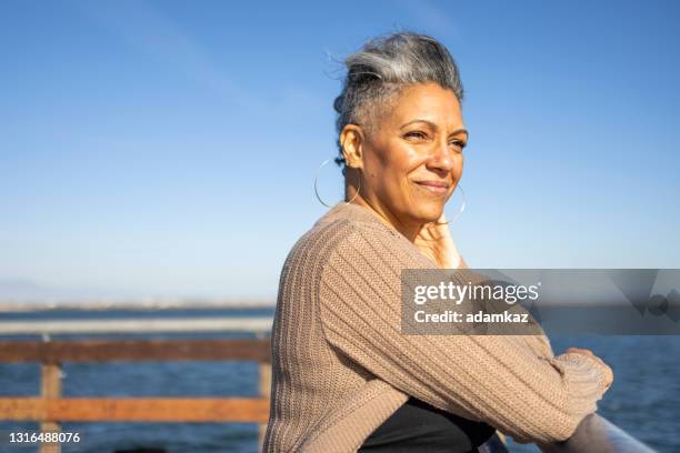 reife schwarze frau entspannen donerisch am pier - happy contemplation stock-fotos und bilder