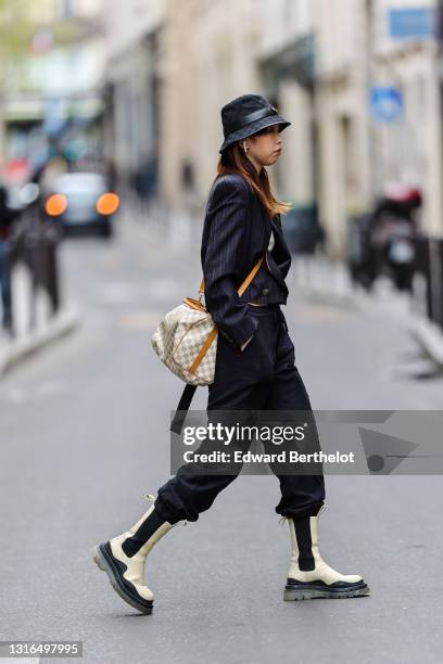 Passerby wears a black fabric Gucci Monogram bob hat with a black shiny leather 'GG' gold buckle belt, a white ribs t-shirt, a black and brown...