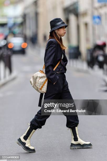 Passerby wears a black fabric Gucci Monogram bob hat with a black shiny leather 'GG' gold buckle belt, a white ribs t-shirt, a black and brown...