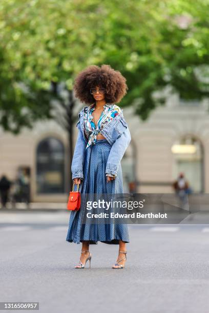 Alicia Aylies wears silver Gucci sunglasses, a silver chains necklace, a white and blue pattern silk knotted Roberto Cavalli shirt, a blue faded...