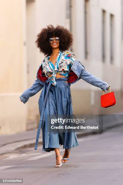 Alicia Aylies wears silver Gucci sunglasses, a silver chains necklace, a white and blue pattern silk knotted Roberto Cavalli shirt, a blue faded...