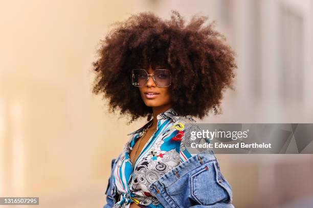 Alicia Aylies wears silver Gucci sunglasses, a silver chains necklace, a white and blue pattern silk knotted Roberto Cavalli shirt, a blue faded...