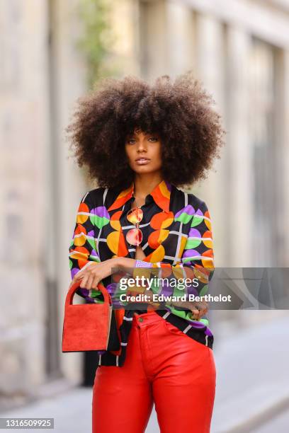 Alicia Aylies wears red and gold Bottega Veneta sunglasses, a gold chain pendant necklace, a black with red orange purple and green pattern Lanvin...