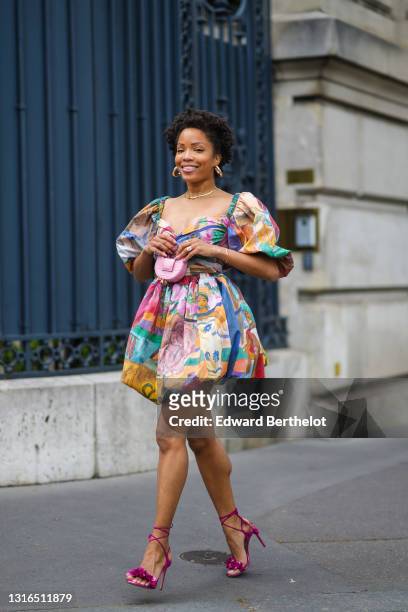 Ellie Delphine wears gold earrings, a gold necklace, a multicolor pattern V-neck with puffy sleeves and skirt short Stella Jean dress, gold rings, a...
