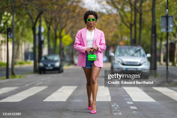 Ellie Delphine wears neon green Versace sunglasses, gold earrings, a gold chain necklace, a white crop tank top, a pink Filkk oversized blazer...