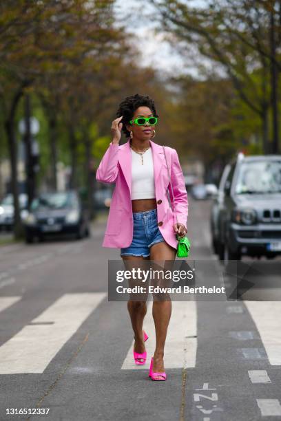 Ellie Delphine wears neon green Versace sunglasses, gold earrings, a gold chain necklace, a white crop tank top, a pink Filkk oversized blazer...