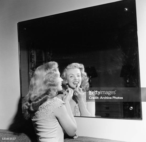American actress Marilyn Monroe puts on her lipstick in a mirror during a visit to the home of Virginia Mcallister in Warrenburg, New York, June...