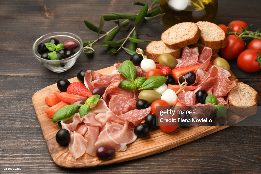 Charcuterie board salami, prosciutto, with green and black olives, appetizers with mozzarella balls, cherry tomatoes and strawberries.
